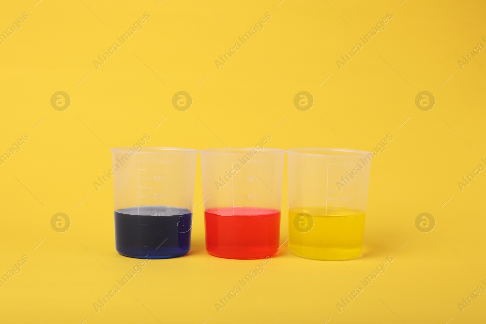 Photo of Beakers with colorful liquids on yellow background. Kids chemical experiment set