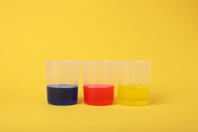Beakers with colorful liquids on yellow background. Kids chemical experiment set