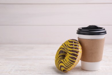 Photo of Tasty donut and cup of hot drink on white wooden table, space for text