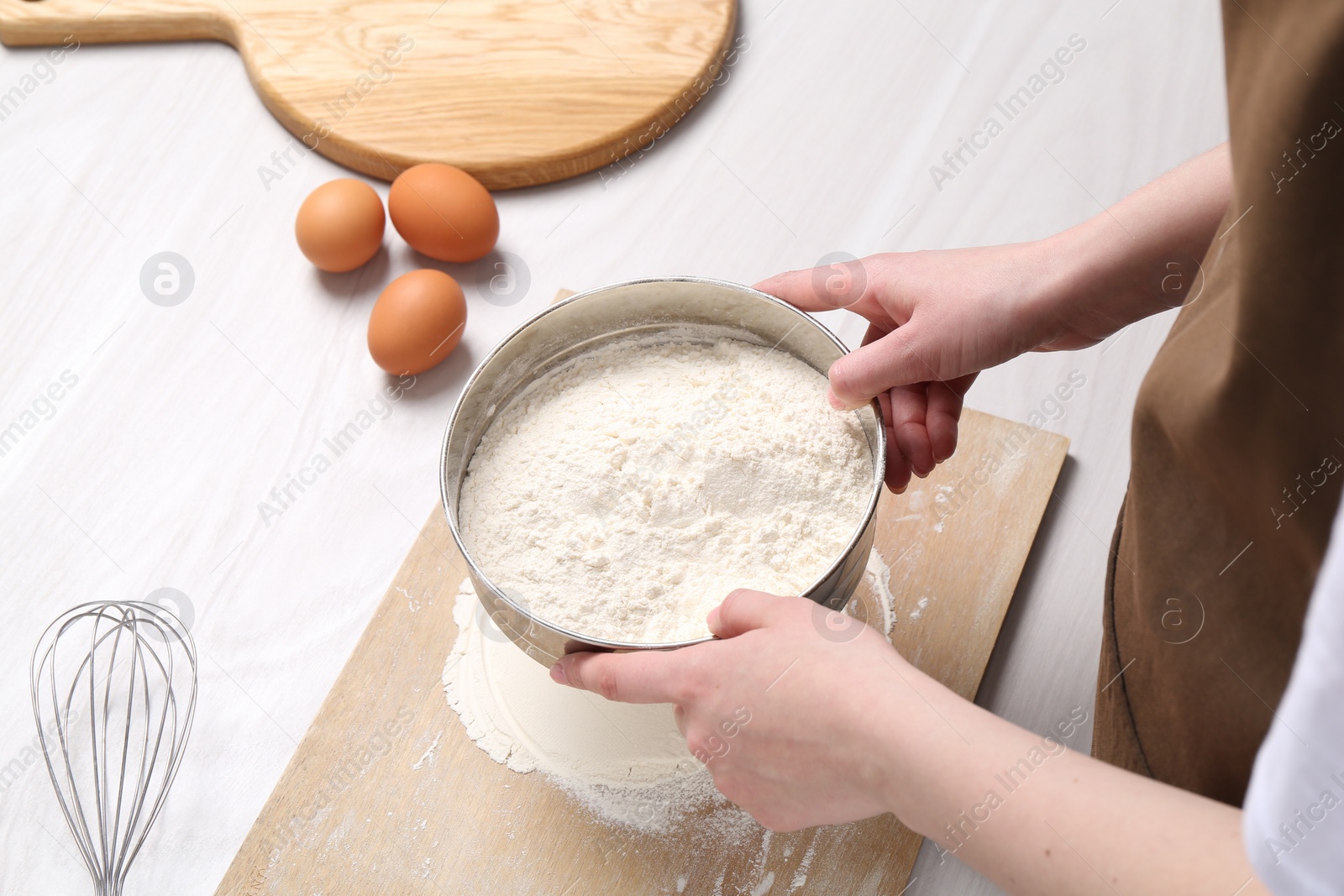 Photo of Woman sieving flour at white wooden table, above view