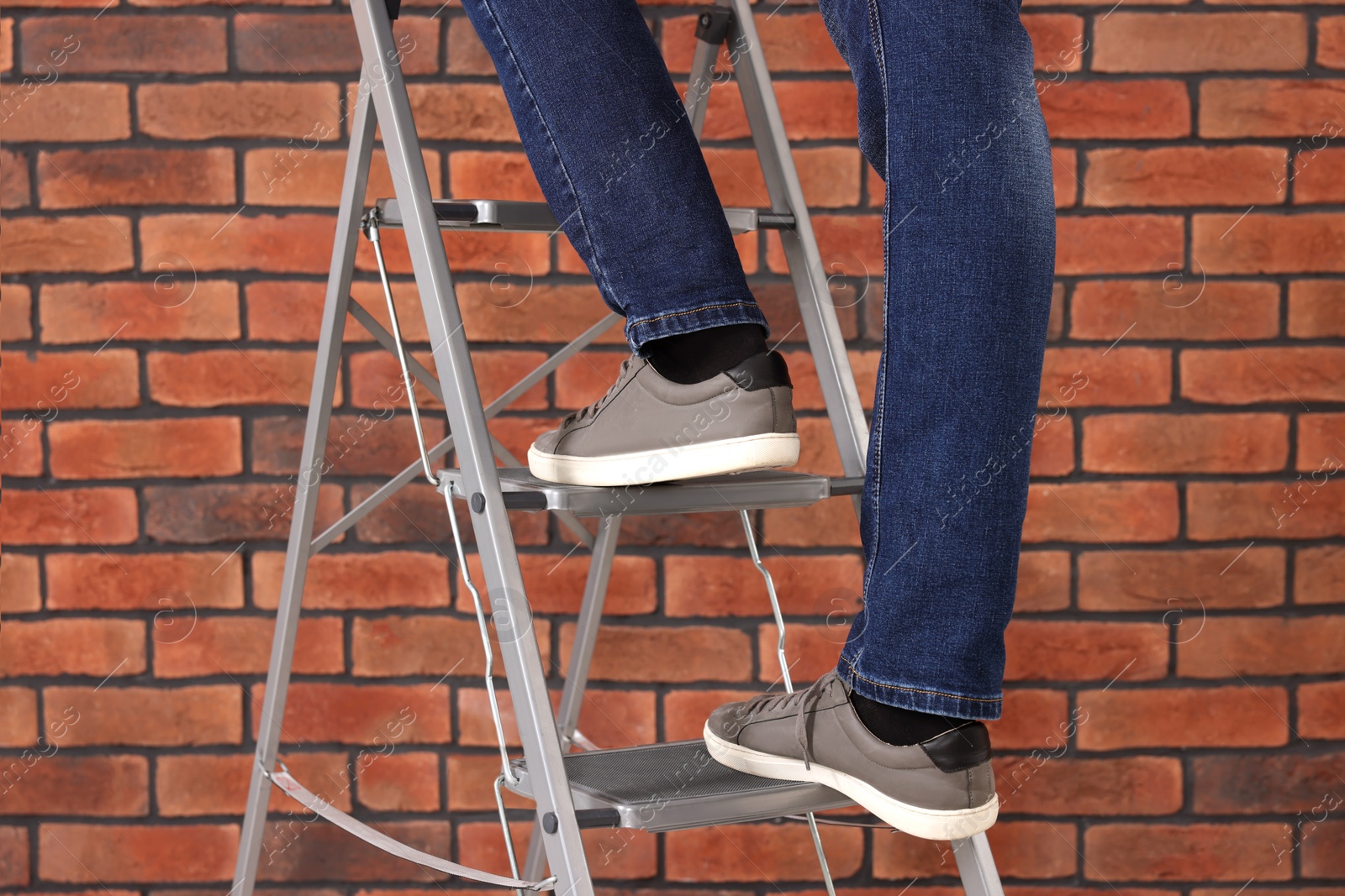 Photo of Man climbing up metal stepladder near brick wall, closeup