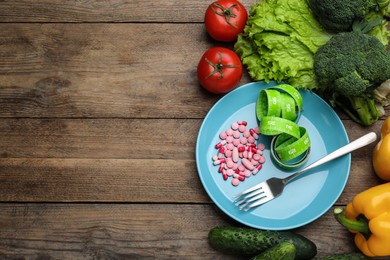 Photo of Plate with weight loss pills, measuring tape, fork and different vegetables on wooden table, flat lay. Space for text