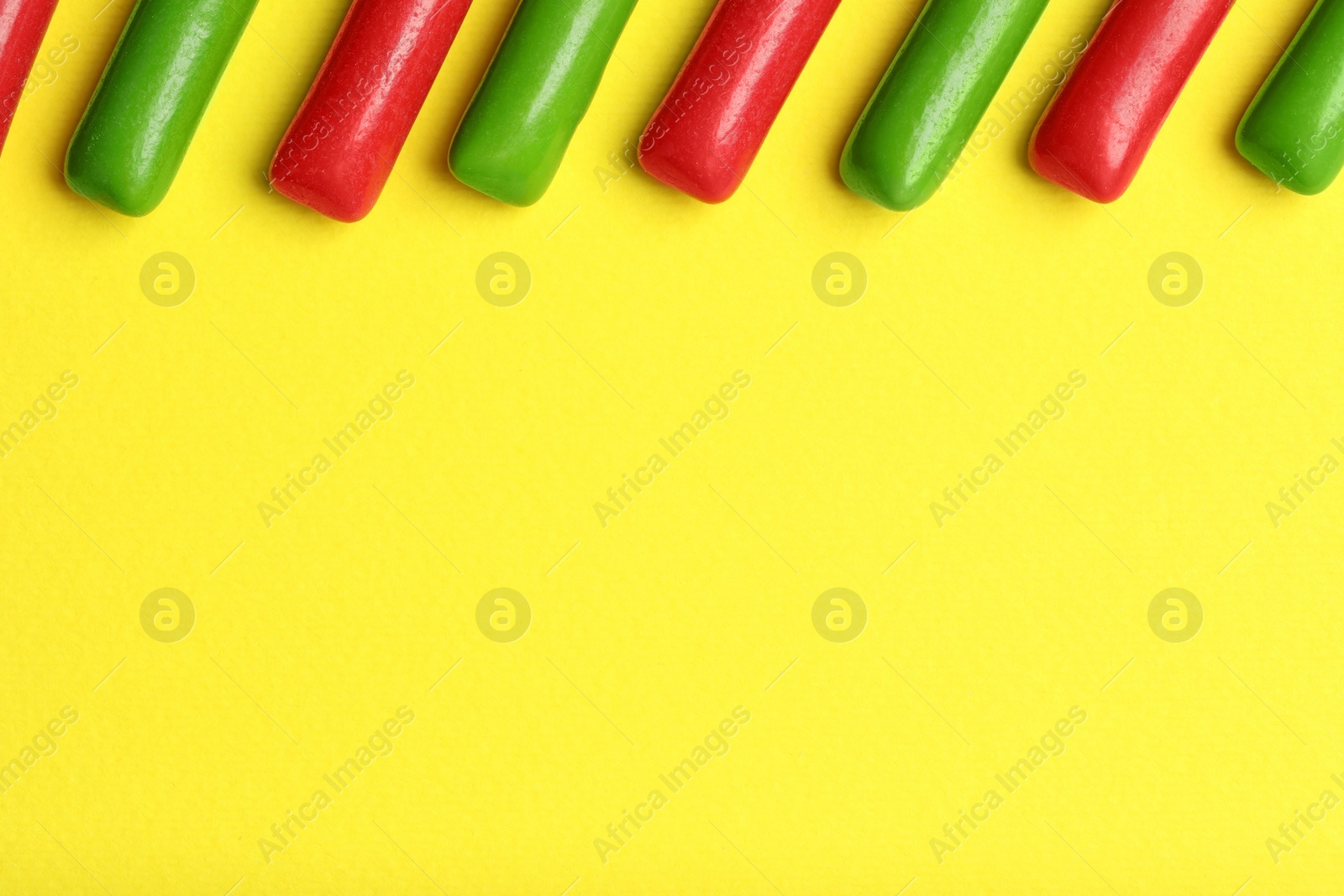 Photo of Many tasty bubble gums on yellow background, flat lay. Space for text