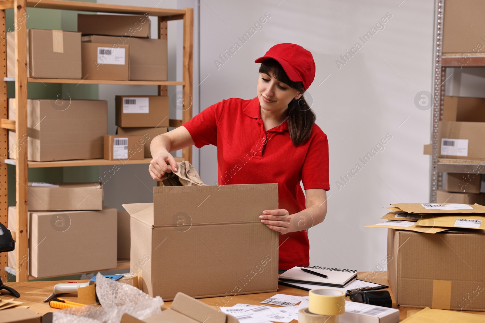 Photo of Post office worker packing parcel at wooden table indoors