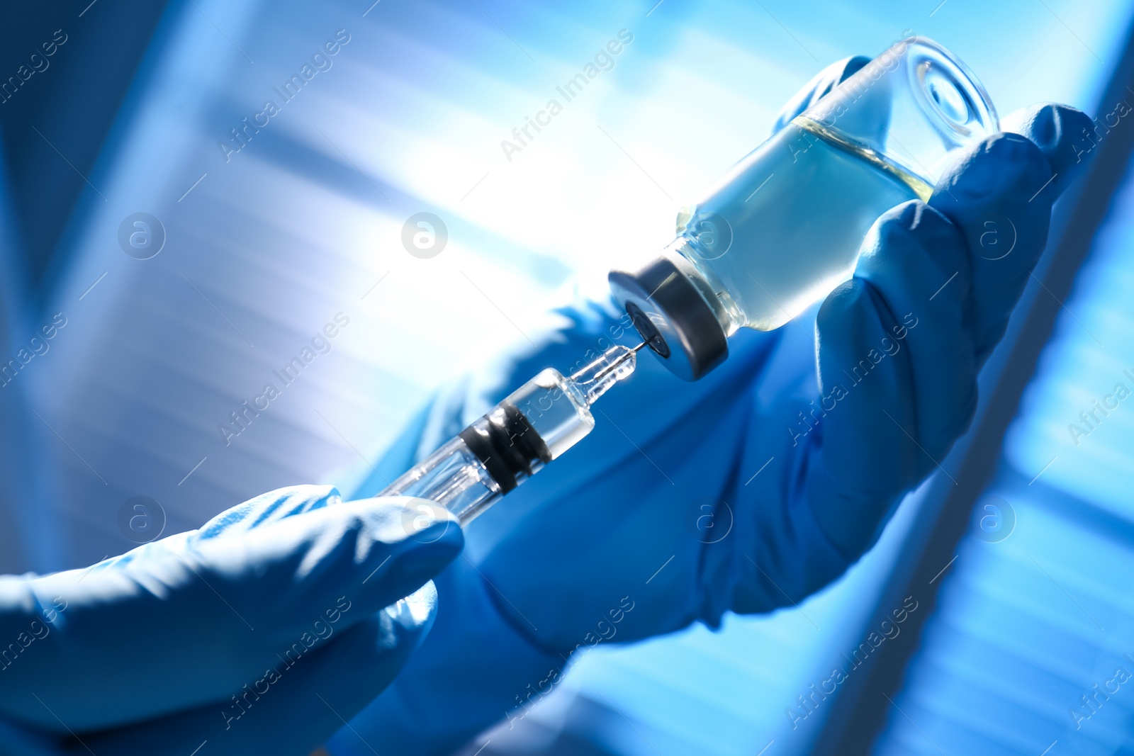 Photo of Woman filling syringe with vaccine from vial on blurred background, closeup