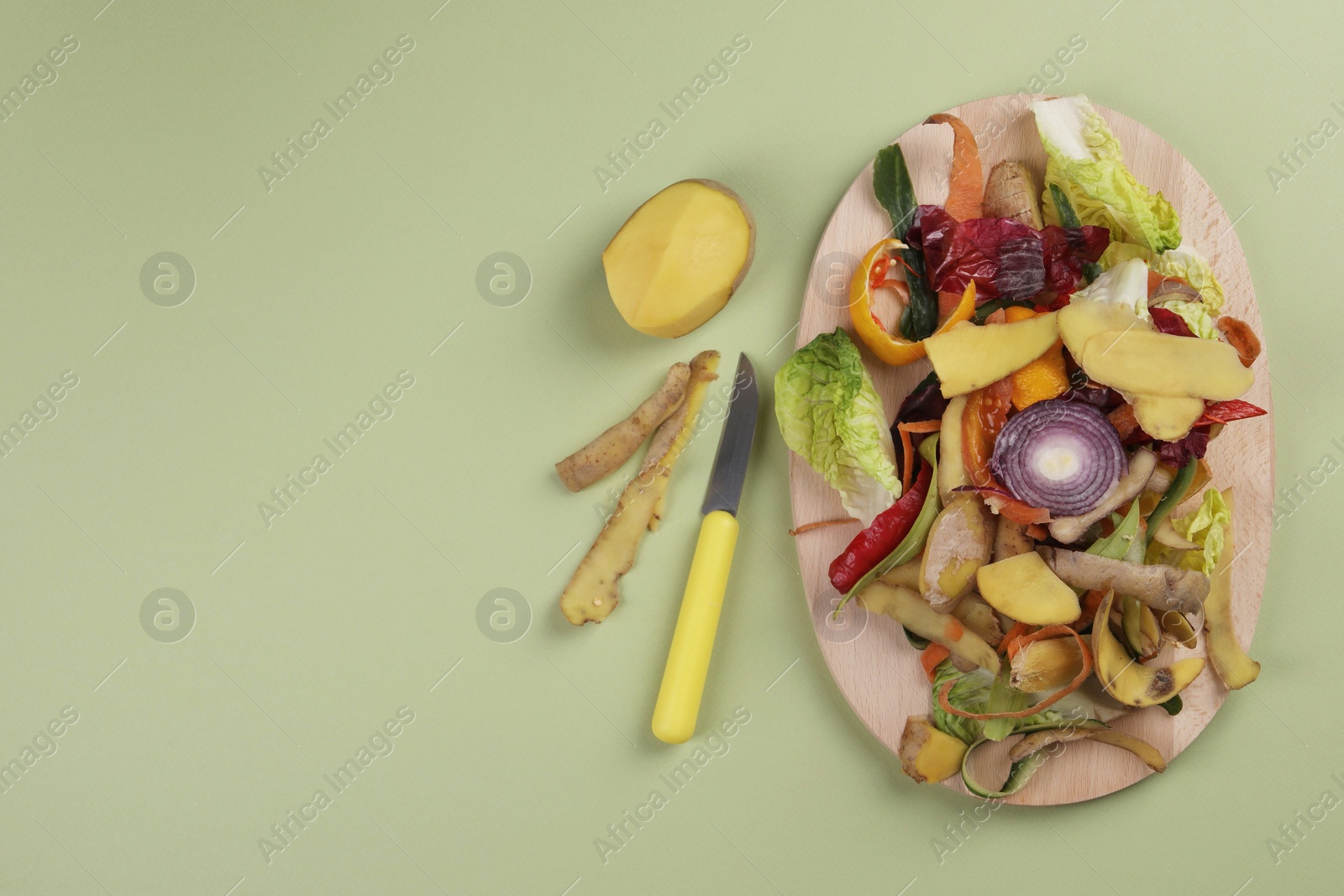 Photo of Peels of fresh vegetables and knife on light green background, flat lay. Space for text