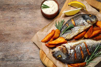 Delicious roasted fish and potatoes on wooden table, flat lay. Space for text