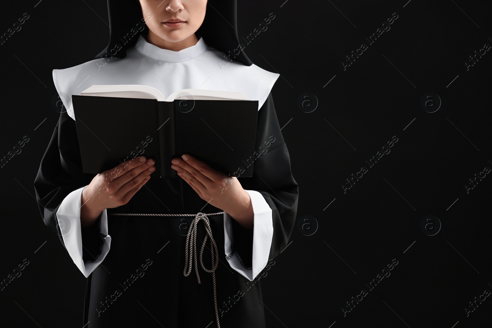 Photo of Nun reading Bible on black background, closeup. Space for text