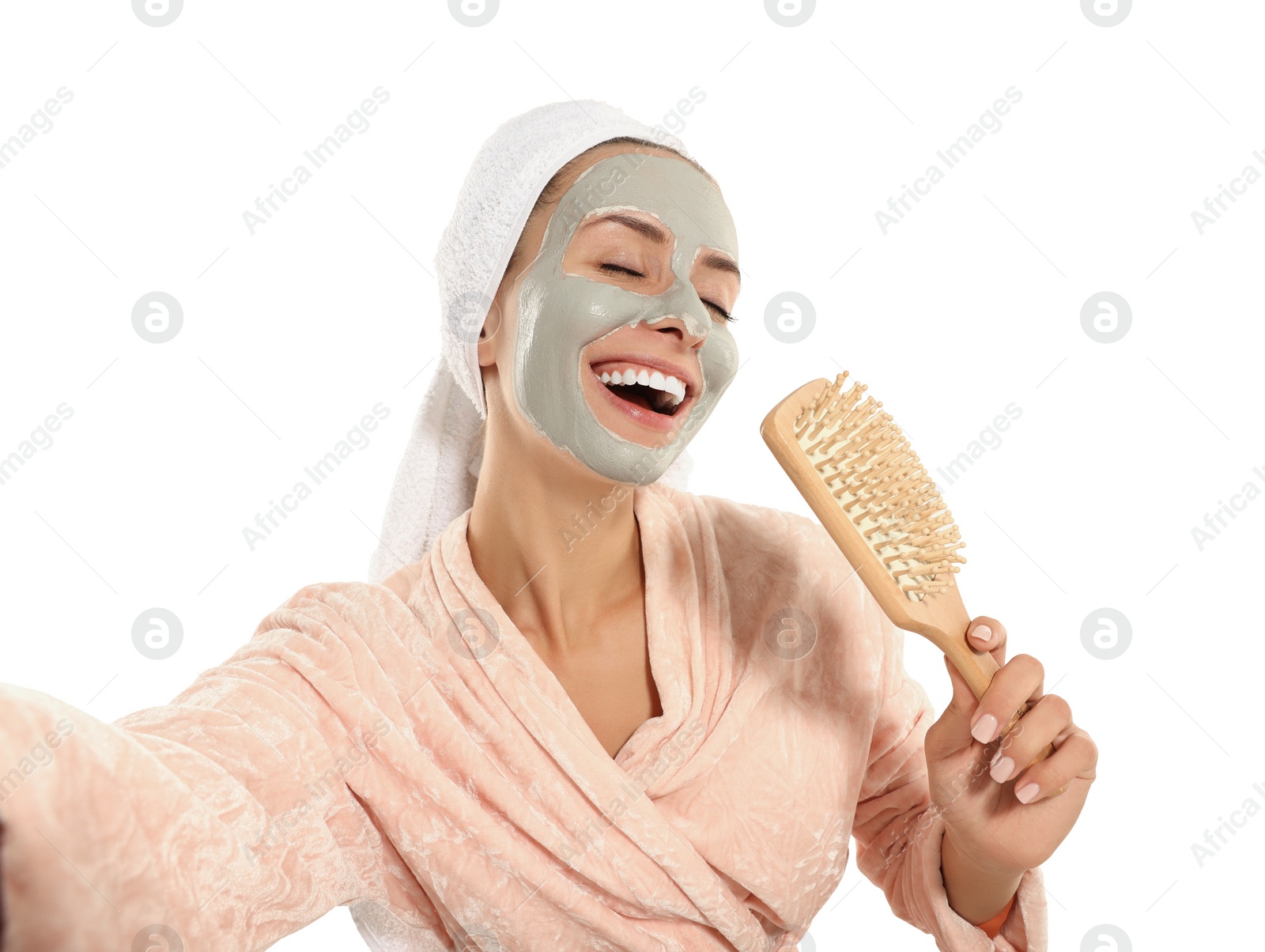 Photo of Woman with face mask and brush singing while taking selfie on white background. Spa treatments