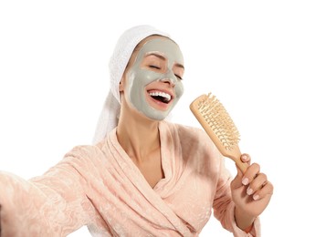 Photo of Woman with face mask and brush singing while taking selfie on white background. Spa treatments
