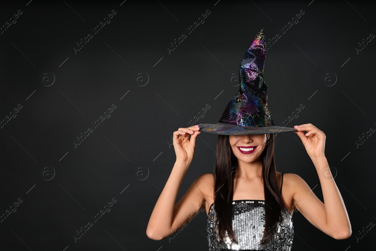 Photo of Beautiful woman wearing witch costume for Halloween party on black background, space for text