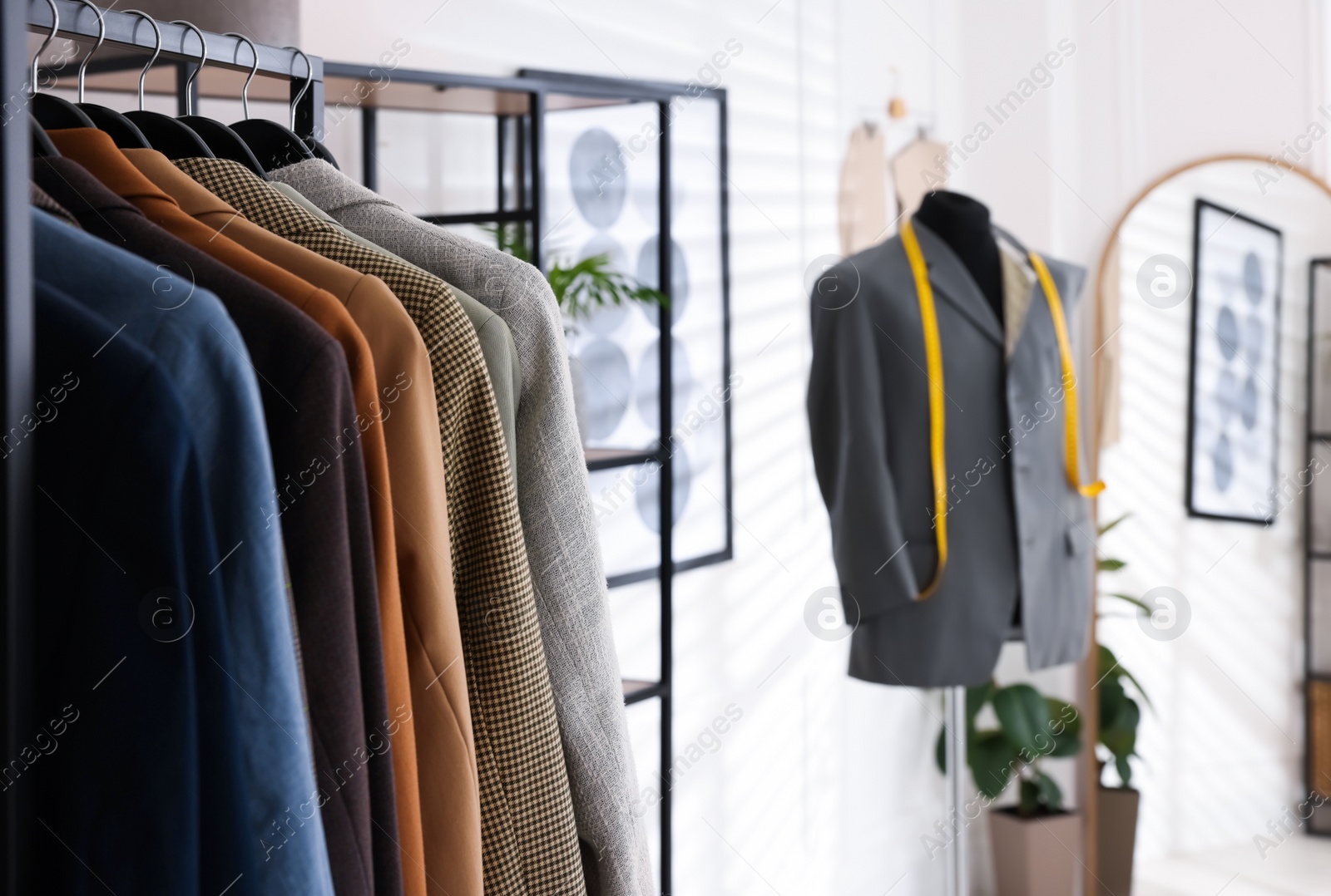 Photo of Rack with male suits and mannequin in tailor shop