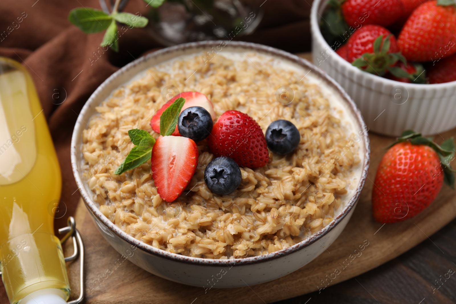 Photo of Tasty oatmeal with strawberries and blueberries in bowl on wooden table, closeup