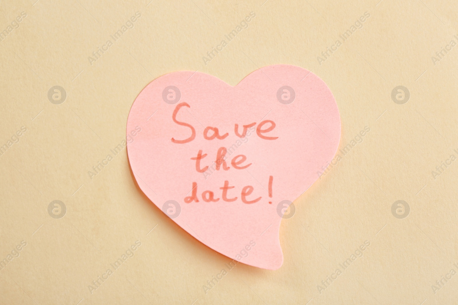 Photo of Heart shaped note with phrase SAVE THE DATE on beige background, top view