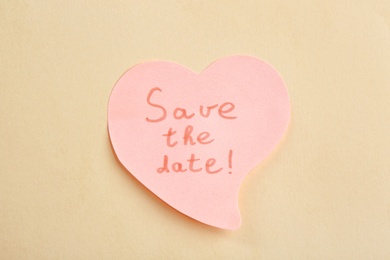 Heart shaped note with phrase SAVE THE DATE on beige background, top view