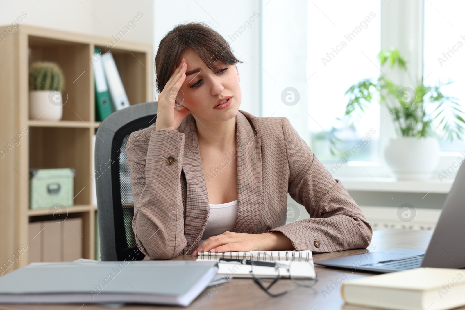 Photo of Overwhelmed office worker sitting at table with laptop indoors