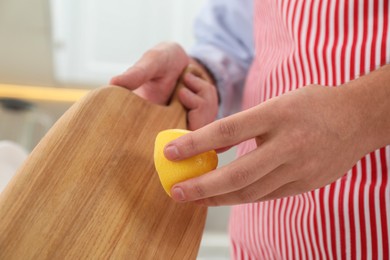 Photo of Man rubbing wooden cutting board with lemon at home, closeup