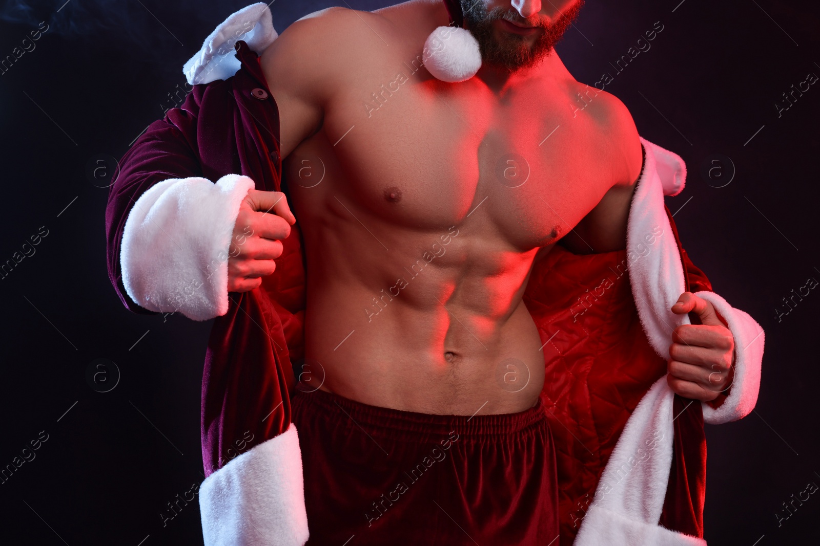 Photo of Attractive young man with muscular body in Santa costume on black background, closeup