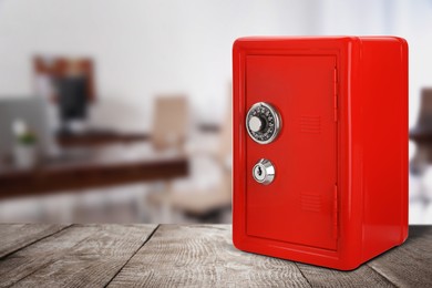 Red closed steel safe with mechanical lock on wooden table indoors. Space for text