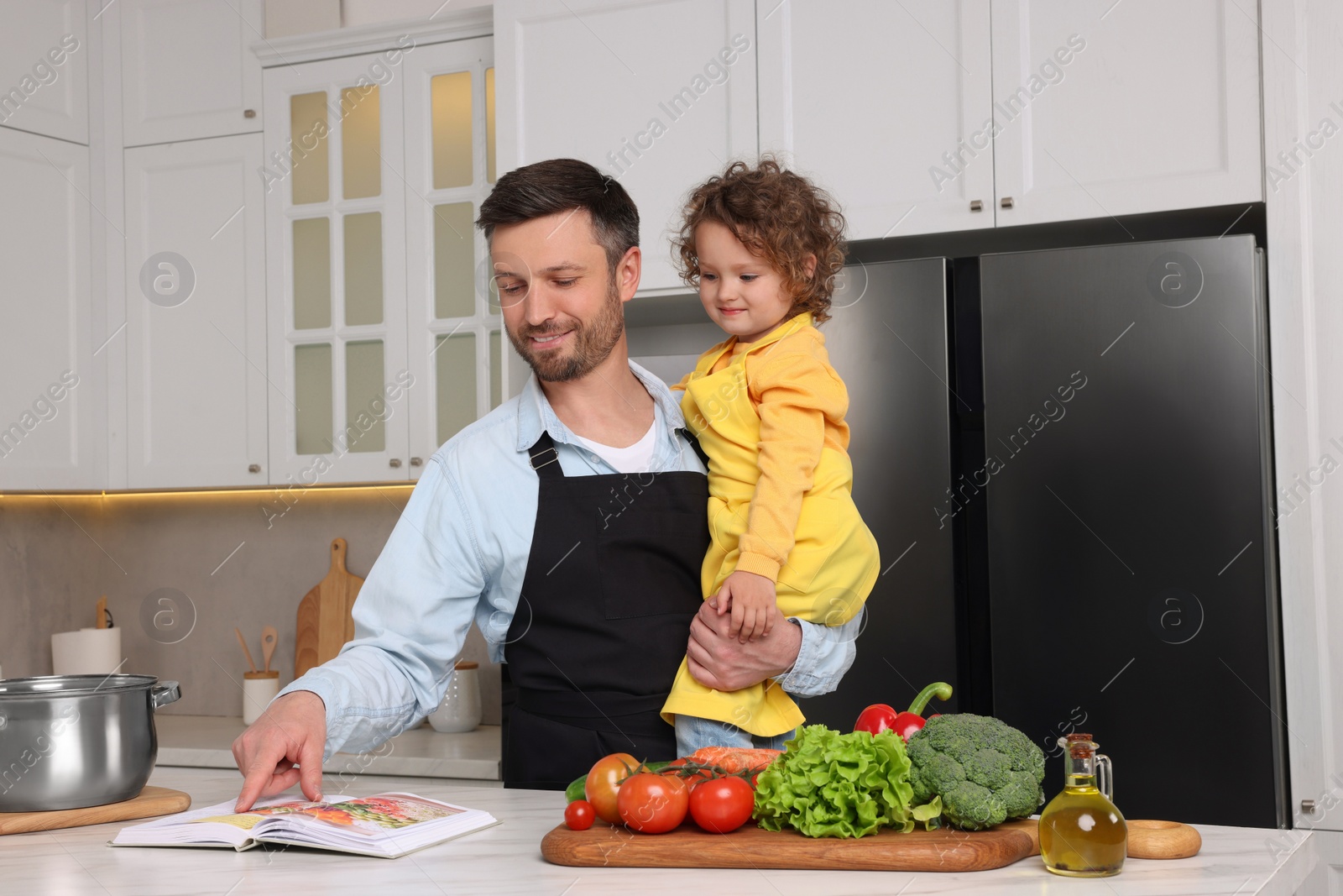 Photo of Cute little girl and her father with recipe book cooking in kitchen