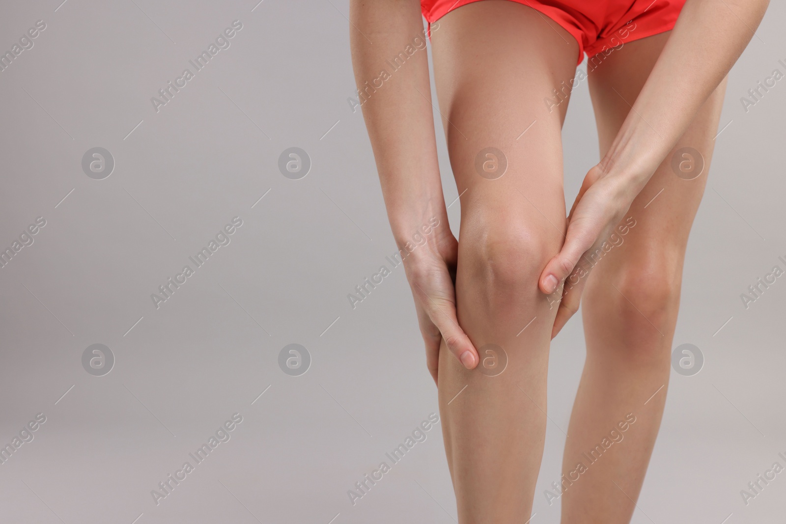 Photo of Woman suffering from leg pain on grey background, closeup. Space for text
