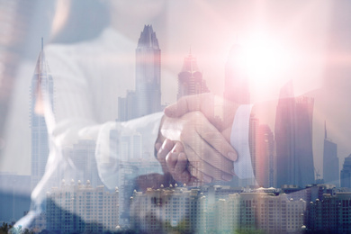 Image of Double exposure of cityscape and business people shaking hands in office, closeup. Team work 