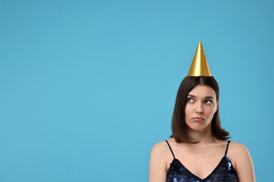 Sad young woman in party hat on light blue background