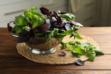 Photo of Metal colander with different fresh basil leaves on wooden table indoors