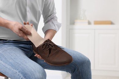 Photo of Man putting orthopedic insole into shoe indoors, closeup. Space for text