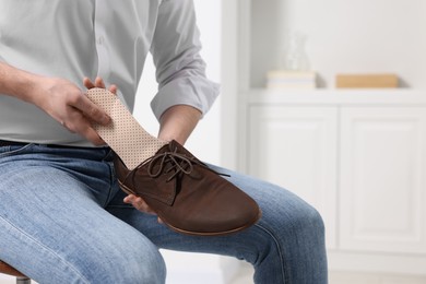 Man putting orthopedic insole into shoe indoors, closeup. Space for text