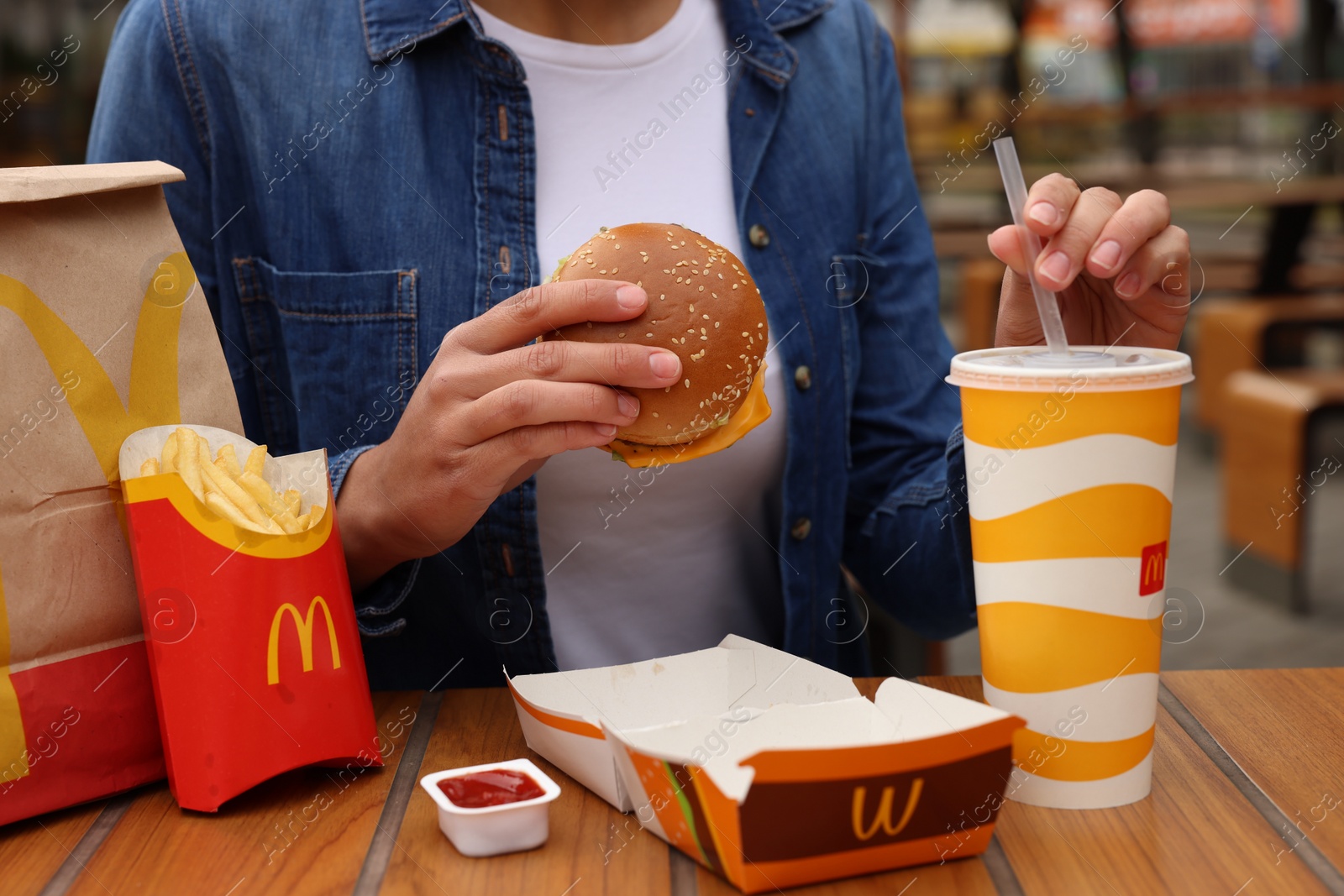 Photo of Lviv, Ukraine - October 9, 2023: Woman with McDonald's menu at wooden table outdoors, closeup