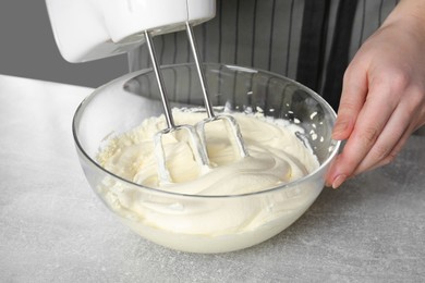 Photo of Woman whipping white cream with mixer at light grey table, closeup