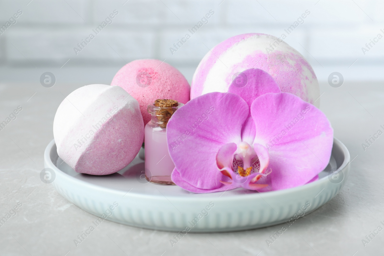 Photo of Colorful bath bombs, bottle of oil and orchid flower on grey table, closeup