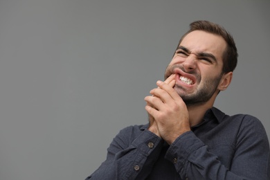 Young man suffering from strong tooth pain on grey background, space for text