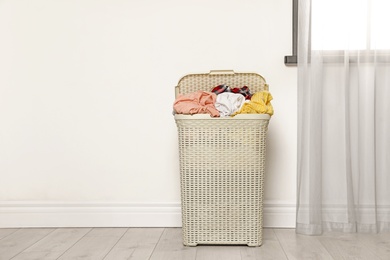 Plastic laundry basket full of dirty clothes on floor near light wall in room. Space for text