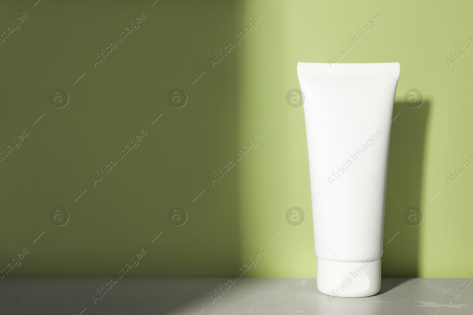 Photo of Tube of face cleansing product on grey table near light green wall. Space for text