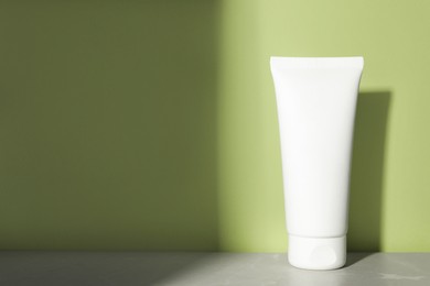 Photo of Tube of face cleansing product on grey table near light green wall. Space for text