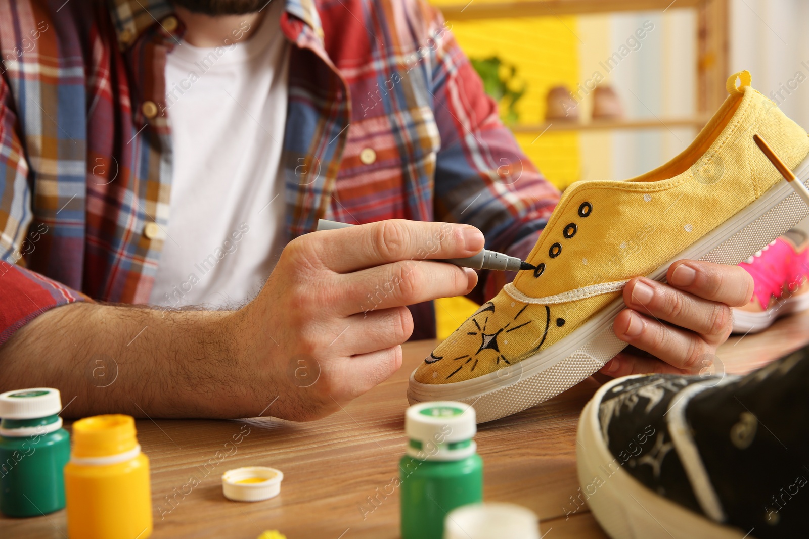 Photo of Man painting on sneaker at wooden table indoors, closeup. Customized shoes