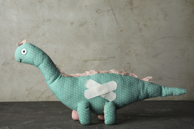 Toy dinosaur with sticking plasters on grey stone table