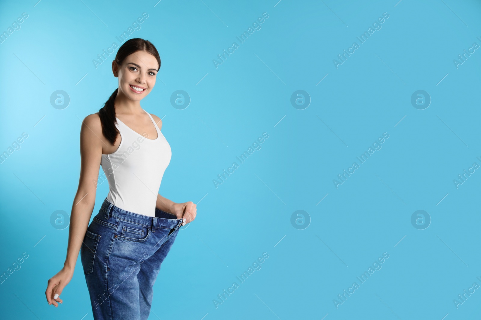 Photo of Attractive young woman with slim body wearing her old big jeans on color background. Space for text