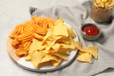 Tasty ketchup with ridged and tortilla chips on grey table