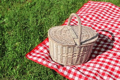 Photo of Picnic basket with checkered tablecloth on green grass outdoors