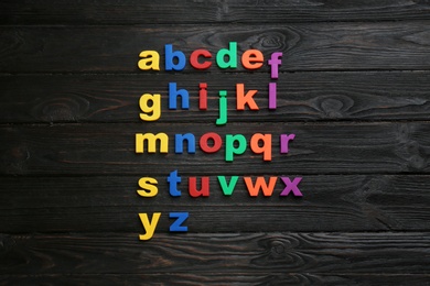 Colorful magnetic letters on black wooden background, flat lay. Alphabetical order