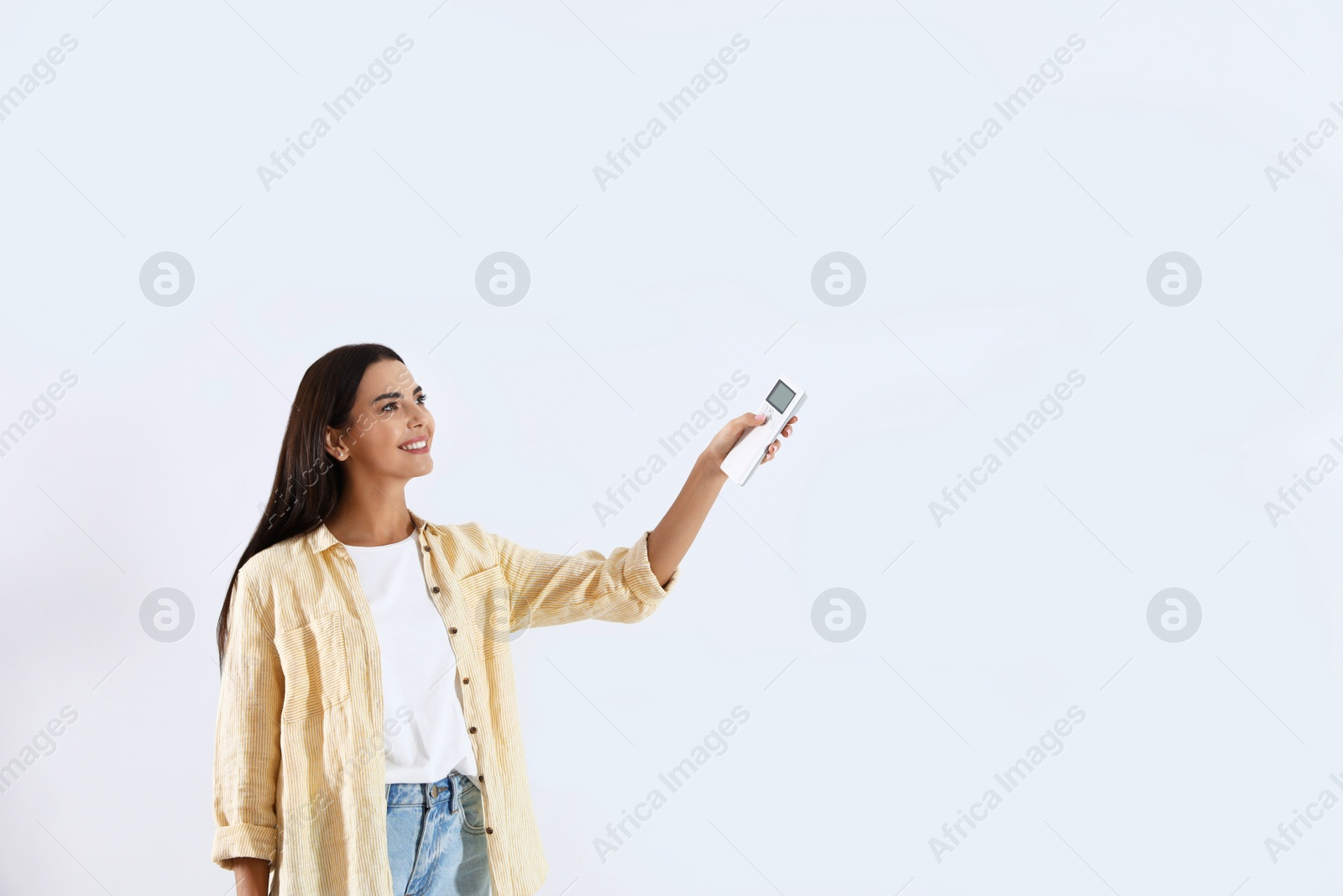 Photo of Young woman turning on air conditioner against white background