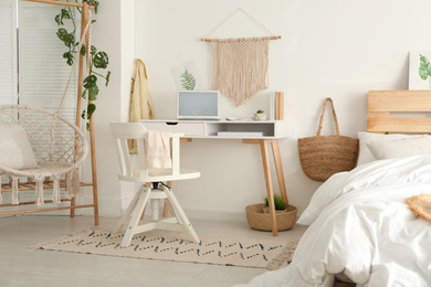 Stylish room interior with workplace, hanging chair and bed