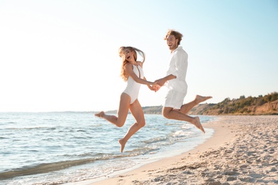 Photo of Happy young couple jumping near sea on beach