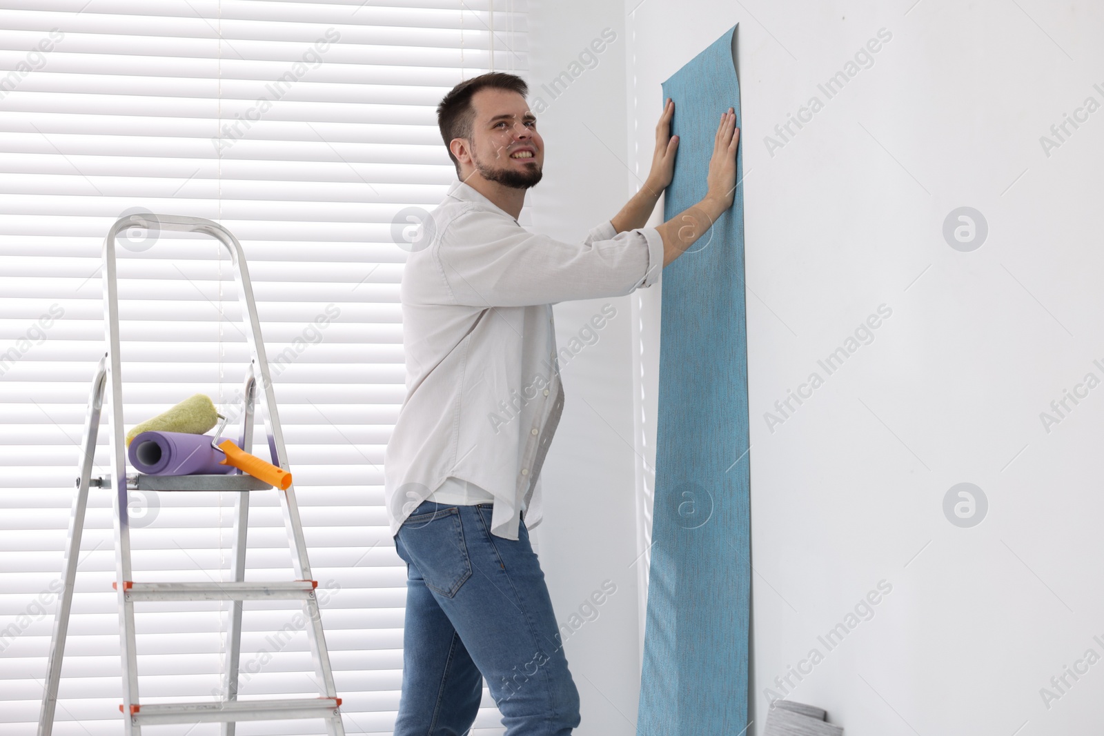 Photo of Man hanging light blue wallpaper in room