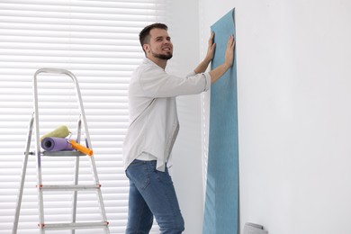 Man hanging light blue wallpaper in room