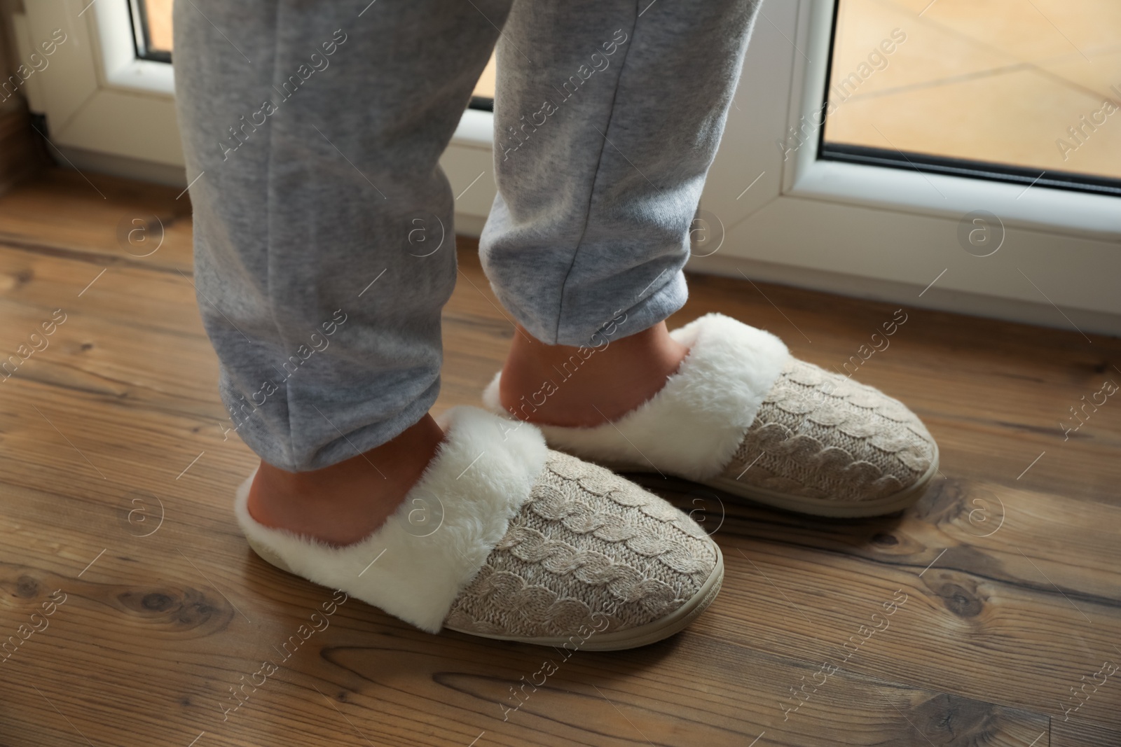 Woman wearing warm beige slippers on wooden floor, closeup Photo of Woman wearing warm beige slippers on wooden floor, closeup