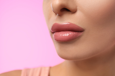 Woman with glossy lipstick on pink background, closeup